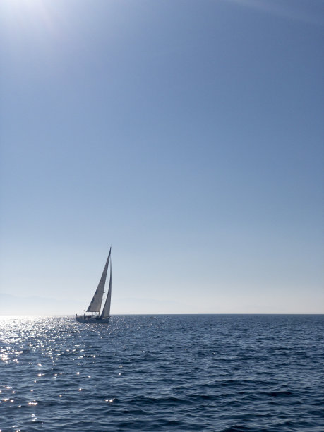 孤独的白色帆船，蓝色的天空和大海的背景，复制空间，垂直图片下载