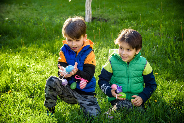 孩子们在春天盛开的花园里寻找复活节彩蛋。孩子们在花丛中寻找五颜六色的蛋。蹒跚学步的小男孩和他的兄弟朋友小男孩在户外玩耍图片下载