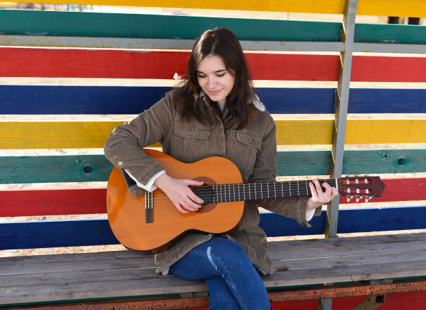 年轻女子弹着吉他，笑着，坐在彩色背景的长椅上图片下载