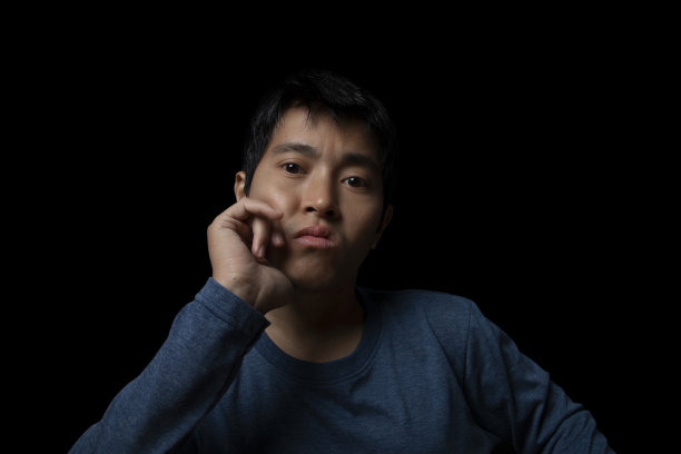 一个年轻人因为黑色背景上的抑郁问题而感到无聊。图片下载