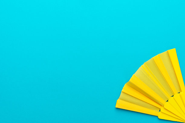 极简主义照片黄色手扇在蓝绿色背景与复制空间图片下载