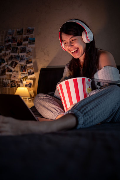 戴着耳机的女人坐在床上吃爆米花看电影图片下载