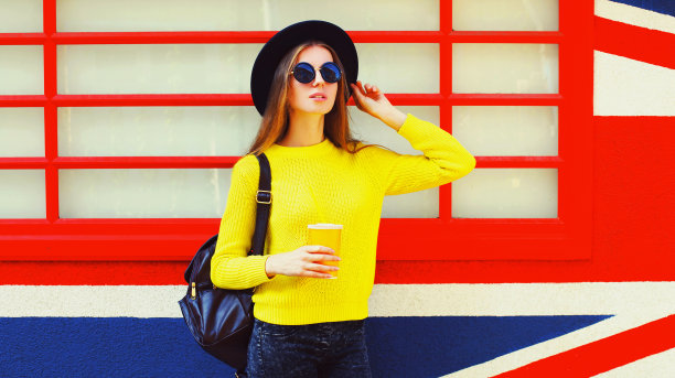 美丽的年轻女子的肖像与一杯果汁在英国国旗墙的背景图片下载