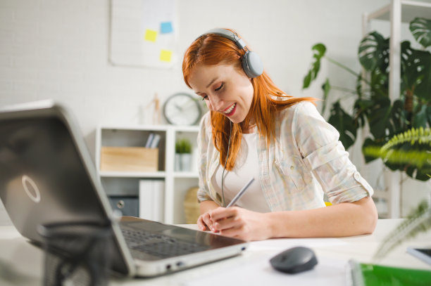年轻漂亮的红发女子戴着耳机在笔记本电脑上在线上课。网络交流，远程学习，在线会议的概念图片下载