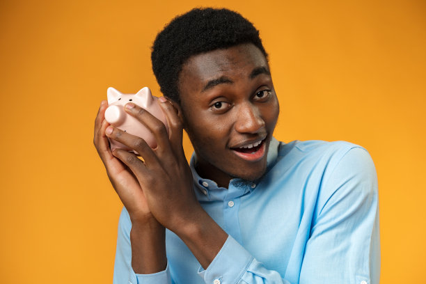 年轻的非裔美国人拿着储蓄罐在黄色背景上图片下载