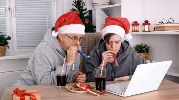 圣诞节期间，戴着圣诞老人帽子的父亲和十几岁的儿子通过笔记本电脑在线会议向亲朋好友祝贺图片下载