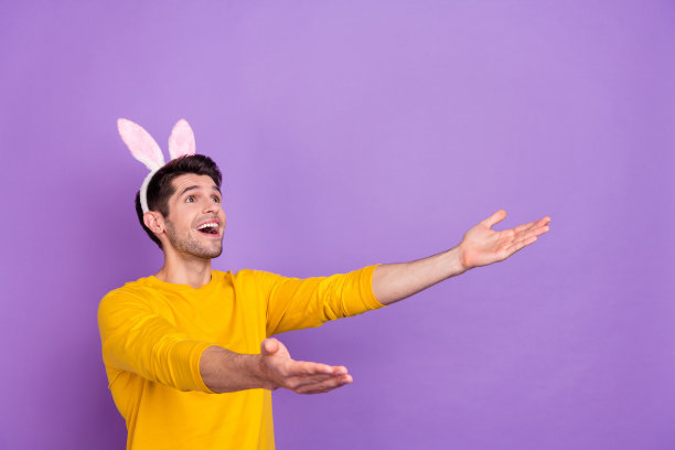好心情的照片，惊讶的疯狂男子与滑稽的兔子耳朵捕捉打折优惠券孤立在紫色的背景图片下载