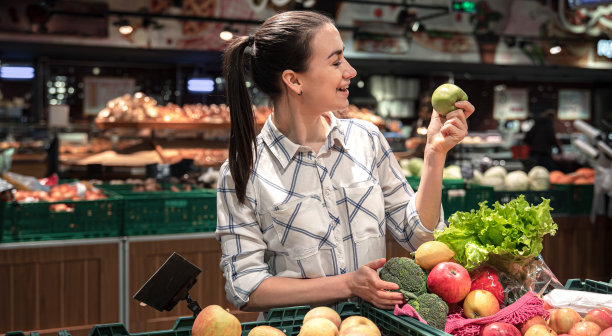一位年轻女子在超市挑选水果和蔬菜。图片下载
