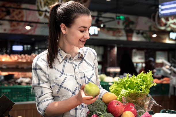 一位年轻女子在超市挑选水果和蔬菜。图片下载