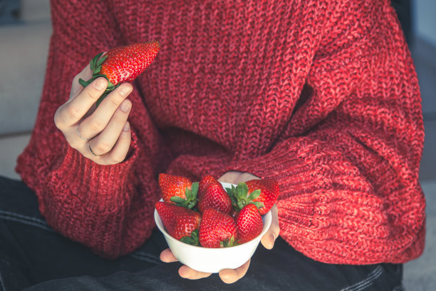 一位身穿红色针织毛衣的妇女手里拿着一盘诱人的草莓。图片下载
