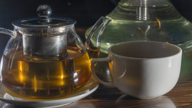 图片玻璃茶壶与陶瓷杯绿茶在黑暗的背景。热的中国绿茶。图片下载