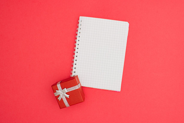 圣诞A6笔记本线装订模拟空白模板设计思路。红色礼物模型对柔和的粉红色背景。复制空间模板设计的新年消息布局。图片下载