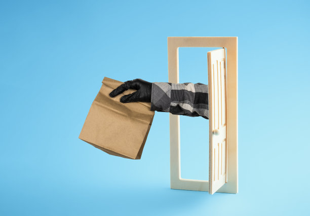 交付的概念。快递员的手拿着纸袋，贴在蓝色背景的门外。图片下载