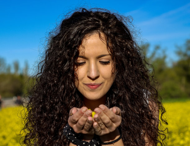 这是一个年轻女孩的特写照片，她手里拿着花，准备在春天的黄花田里吹花图片下载