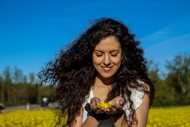 这是一个年轻女孩的特写照片，她手里拿着花，准备在春天的黄花田里吹花图片下载
