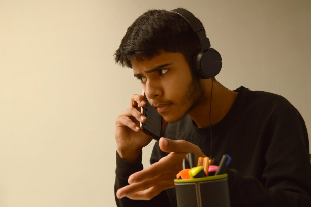 一个年轻的聪明的年轻印度亚裔男孩的水平镜头不高兴或不高兴，表现出沮丧的手势，集中注意力，在灰色的背景下接听或通话，他的头戴耳机图片下载