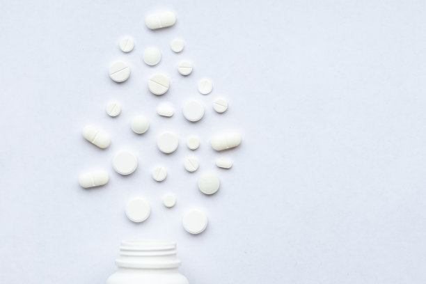 从弹出的塑料瓶中取出一捆不同的药片，平铺在桌子上。白色背景上一堆打开的药物。副本的空间。药物和Phramacy。图片下载