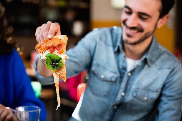 近距离的年轻潮男坐在桌子旁吃着笑着，因为他的披萨里有太多的马苏里拉奶酪。图片下载