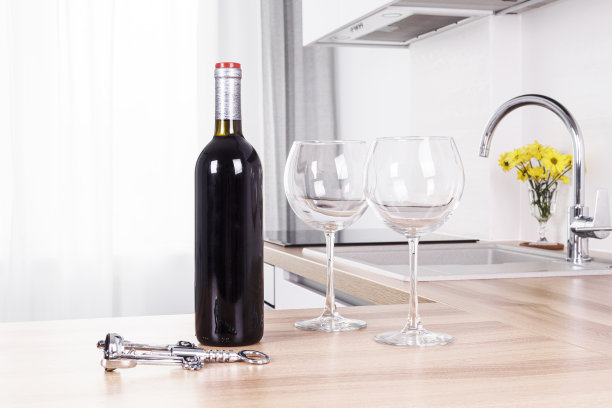 一瓶红酒，两个酒杯，一个开瓶器在厨房的桌子上，一个酒吧在厨房里。舒适的家，浪漫的夜晚。晚餐时喝点酒。光内部。厨房。图片下载