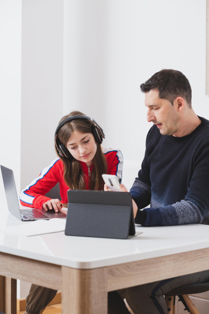 父亲带着智能手机，女儿戴着耳机一起工作。图片下载