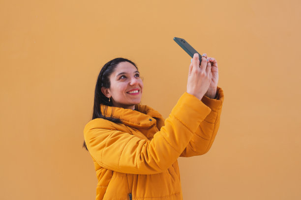 快乐的年轻女子在黄色背景上自拍。图片下载