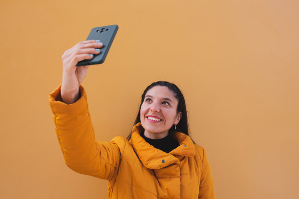 快乐的年轻女子在黄色背景上自拍。图片下载
