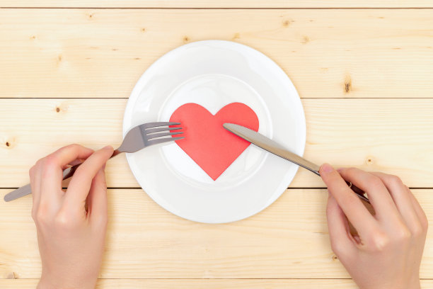 健康饮食。女性手用叉子和餐刀在白色盘子上切一颗红心。俯视图图片下载