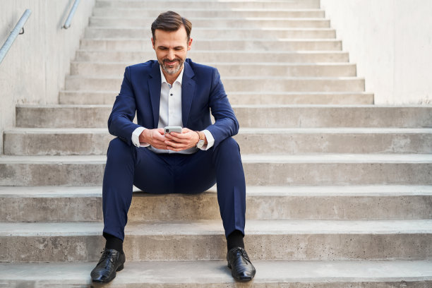 穿着西装，面带微笑的商人坐在城市的楼梯上用手机图片下载