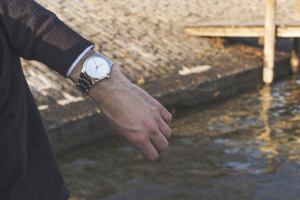 一个男人举手示意时间。背景是码头和水面。时间观念，放松，生活方式。图片下载