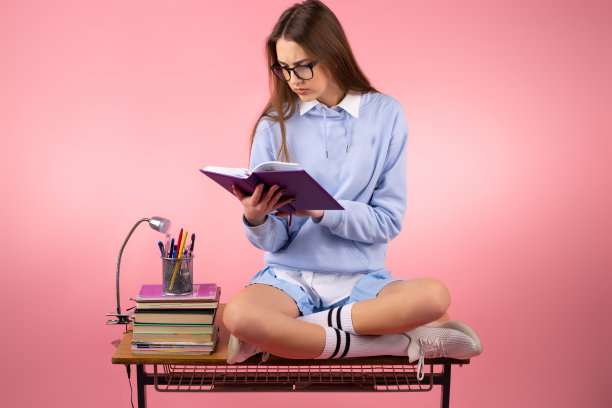 照片中，一名严肃漂亮的女学生，穿着校服，戴着眼镜，正坐在桌子上看书准备上课。图片下载