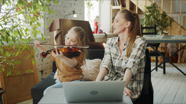 一位女士看着她的女儿演奏音乐。他们用笔记本电脑听课图片下载
