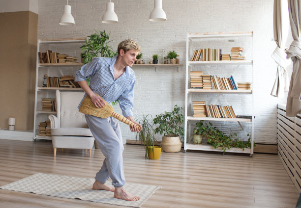 一个快乐的年轻人拿着扫帚载歌载舞，打扫家里的房间。图片下载