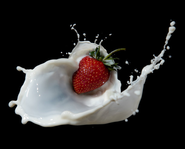 红色的草莓果实落入乳白色的溅在黑色的背景上图片下载