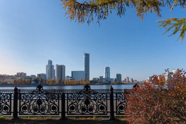 河堤用铸造的镂空格子和秋天的红灌木和落叶松装饰。图片下载