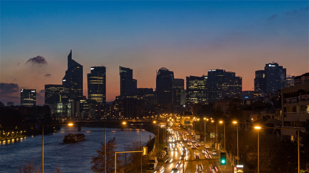 黄昏笼罩在拉德芳斯的天际线上，塞纳河上的小船和道路交通图片下载