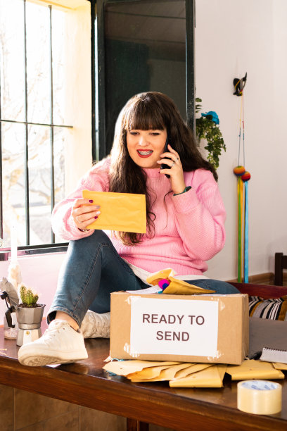 在手工艺车间，女工正坐在桌子上用手机聊天，准备送纸箱的订单图片下载