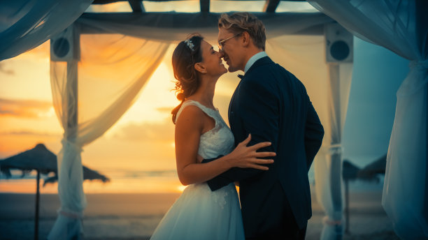 在日落的海洋海滩上，新娘和新郎在户外婚礼上的特写镜头。完美的场所，浪漫的情侣结婚，交换戒指，亲吻和分享庆祝与朋友。图片下载