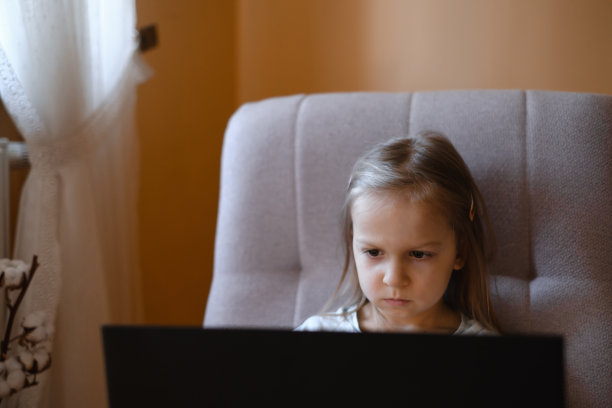 坐在扶手椅上用笔记本电脑看卡通片的孩子图片下载