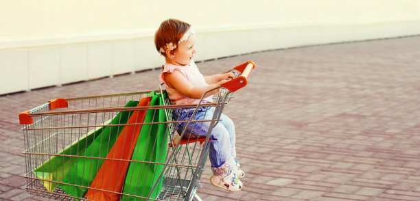 快乐的宝宝拿着购物袋坐在城市的手推车里图片下载