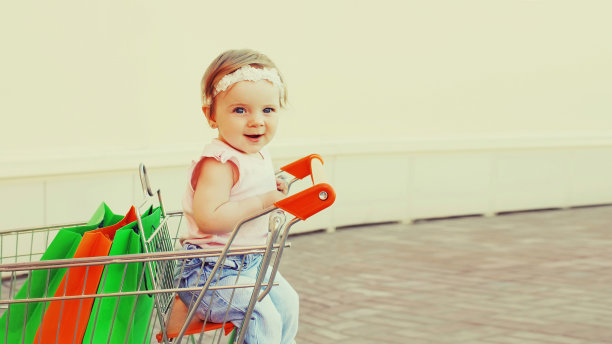 快乐的宝宝拿着购物袋坐在城市的手推车里图片下载