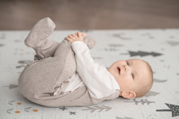 微笑的婴儿躺在他的背部，并把他的手放在他的腿上的垫子上图片下载
