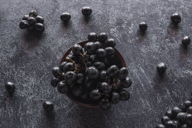 棕色盘子里的黑葡萄，散落在黑色的背景上图片下载