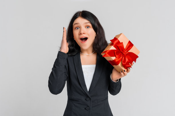快乐兴奋的黑发少女在黑色外套与礼品盒，站在白色背景。节日、庆典、生日理念。年轻的情绪化的女人图片下载