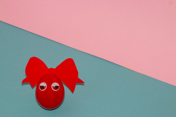 红色的鸡蛋与红色的蝴蝶结和甜蜜的眼睛在柔和的蓝色粉红色背景，创意艺术复活节设计，为设计师复制空间图片下载