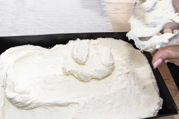 一名妇女将混合的凝乳和鲜奶油倒入烤盘里的烤可可蛋糕。图片下载