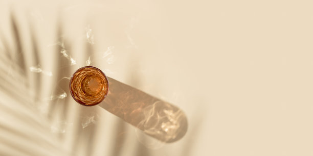 一杯水从彩色玻璃和美丽的阴影从棕榈叶和炫目的阳光，夏季饮料的概念，趋势玻璃橙色，米色背景，审美俯视图图片下载