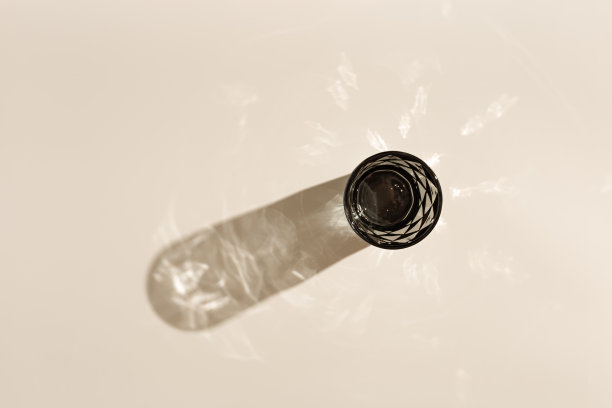 一杯水从着色的灰色玻璃与阳光和眩光的硬阴影，创造性的夏季饮料最小概念，米色背景的现代玻璃，俯视图图片下载