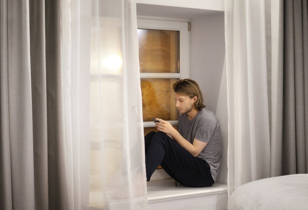 年轻人坐在窗台上玩智能手机图片下载