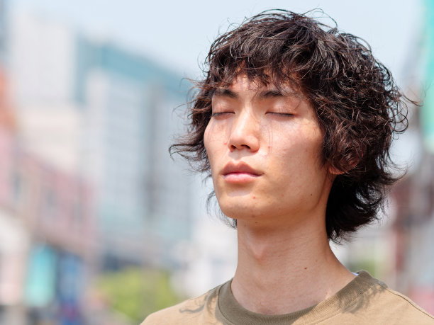 近距离的肖像英俊的中国青年男子与卷曲的黑色头发的眼睛闭在阳光灿烂的夏日。图片下载