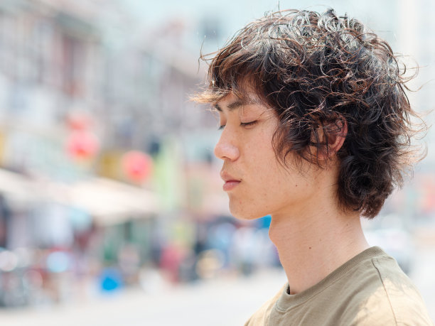 近距离的肖像英俊的中国年轻男子与卷曲的黑色头发眼睛关闭在阳光明媚的夏天，侧视图。图片下载